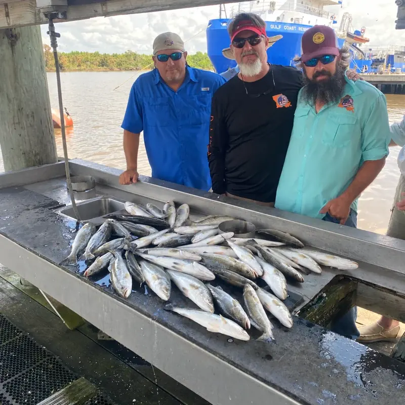 Three clients with their speckled trout catch and water behind them