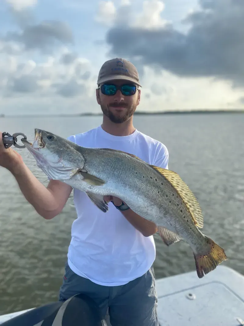 Captain Conlon Brashear wearing a white shirt and holding a large speckled trout