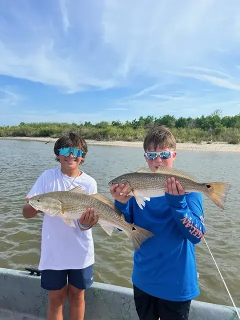 Two young anglers each holding a redfish