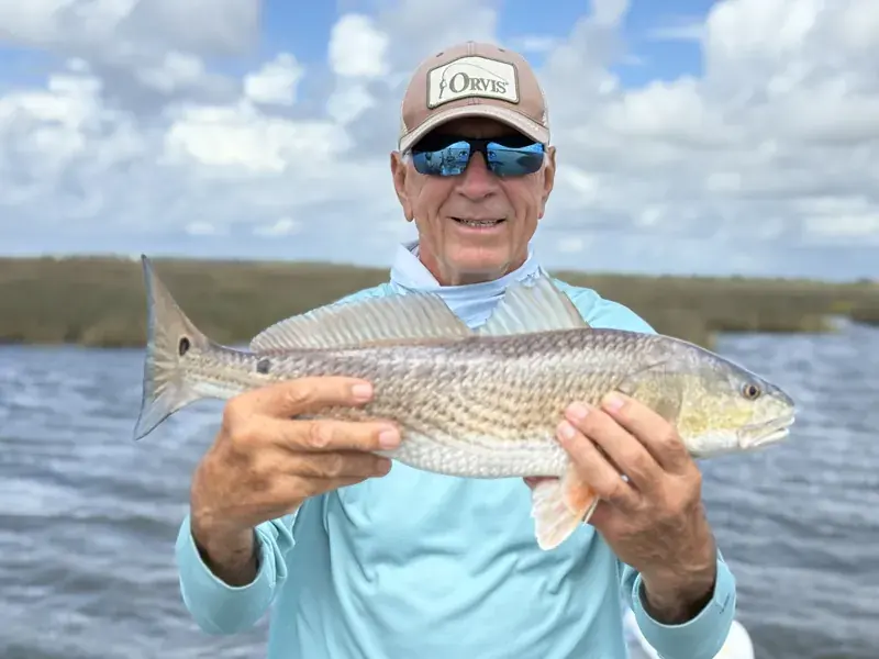 Client wearing an Orvis cap and sunglasses holding a redfish on the water