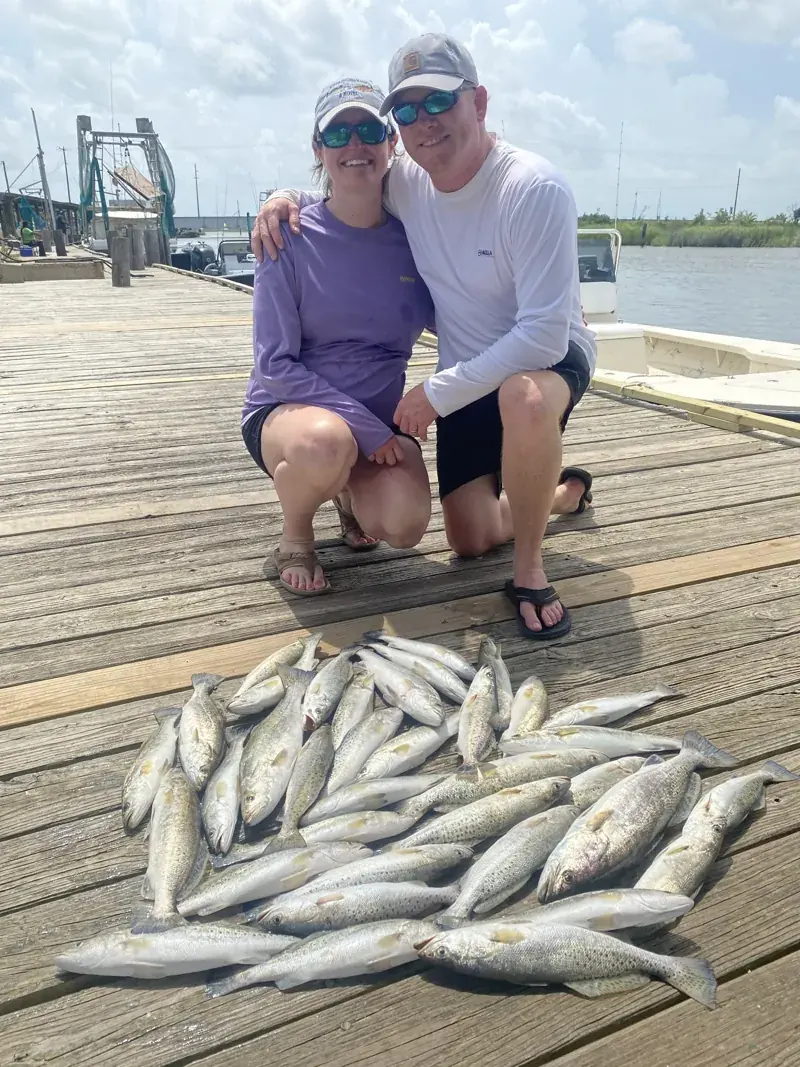 Two clients smiling on the dock beside their speckled trout catch
