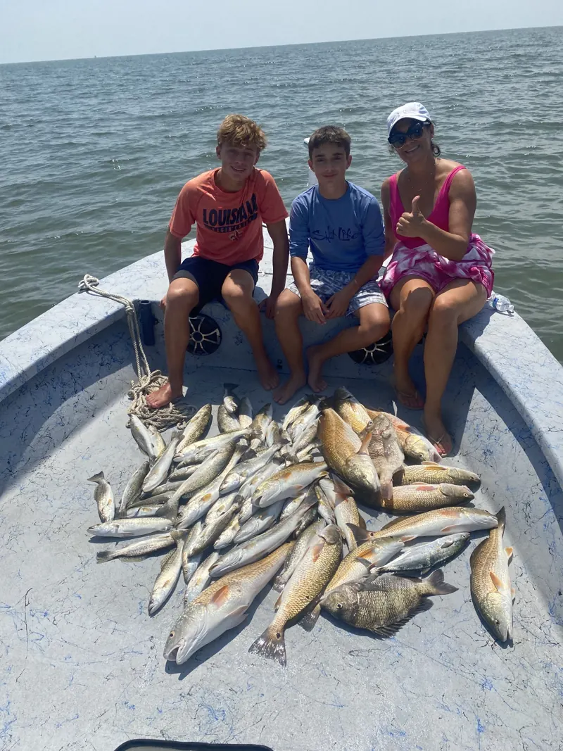 Two boys and their mom giving a thumbs-up beside their catch aboard the boat